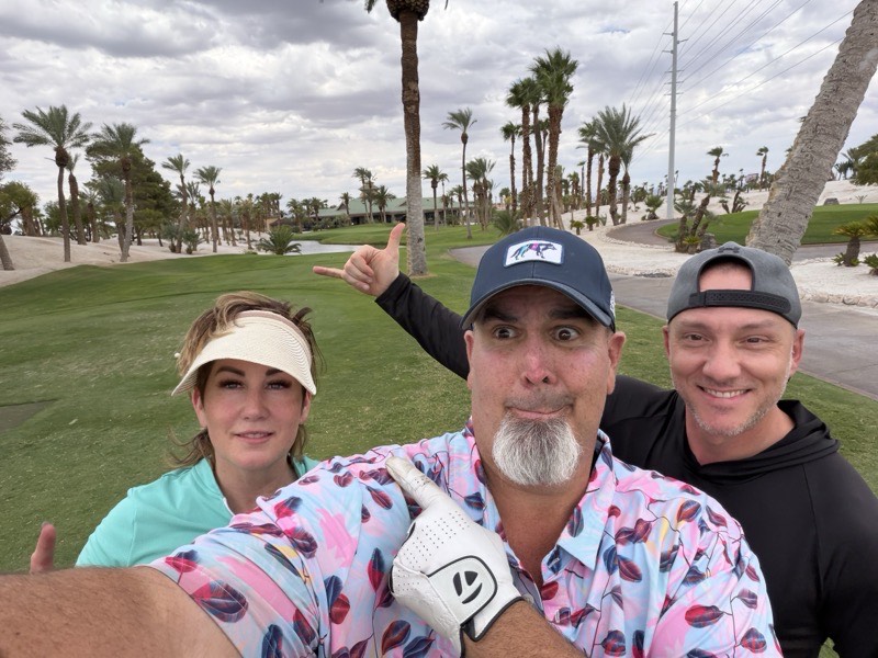 Four people on a golf course under an overcast sky with palm trees.