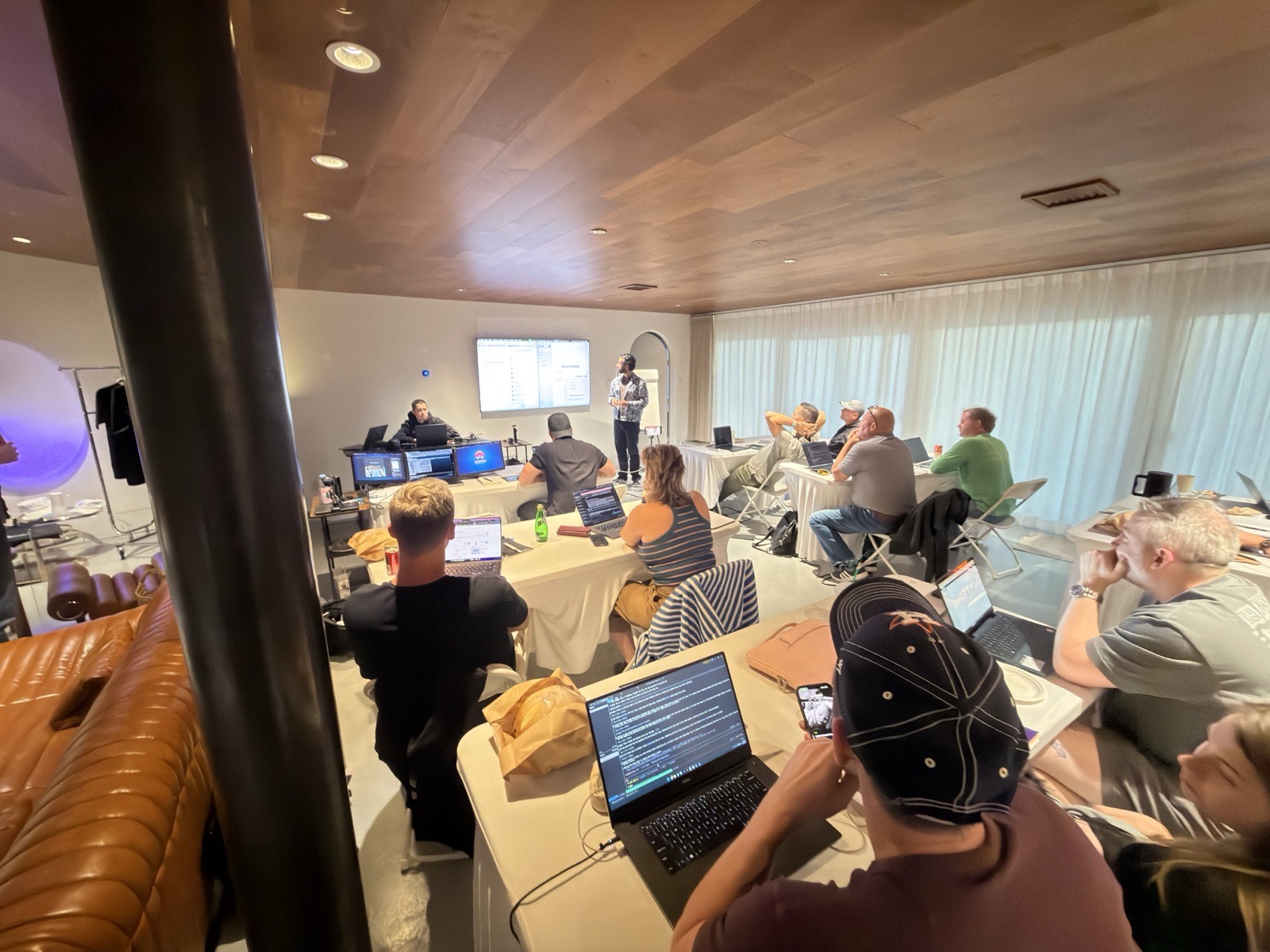A wide view of the working room: people at long tables with laptops open and screens at the front.