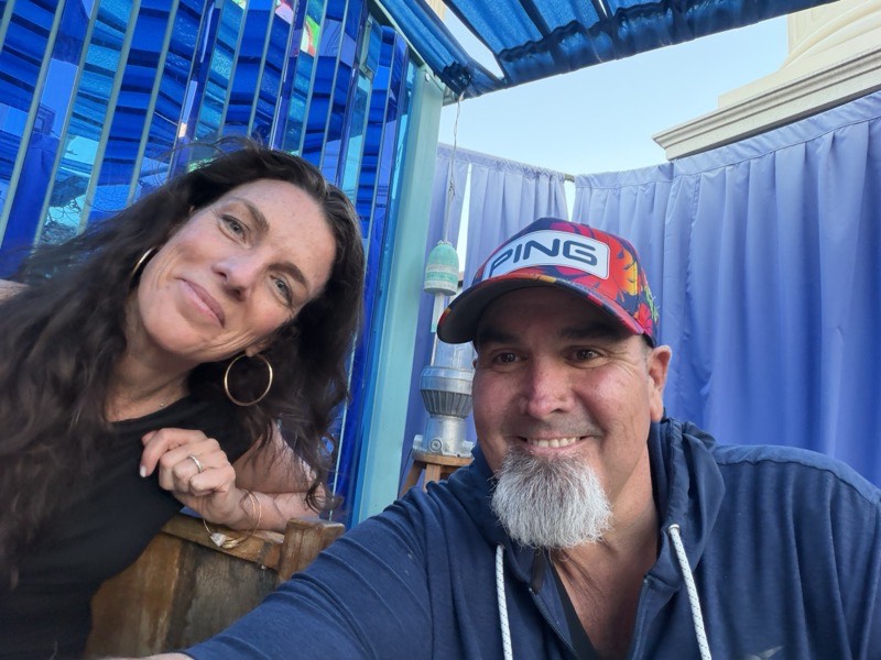 Two people under a blue cabana awning in daylight.
